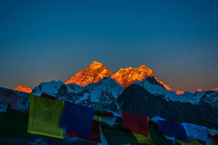 Everest and Lhotse lit orange at sunset above prayer flags on an Everest climbing tour to Everest Base Camp, Nepal