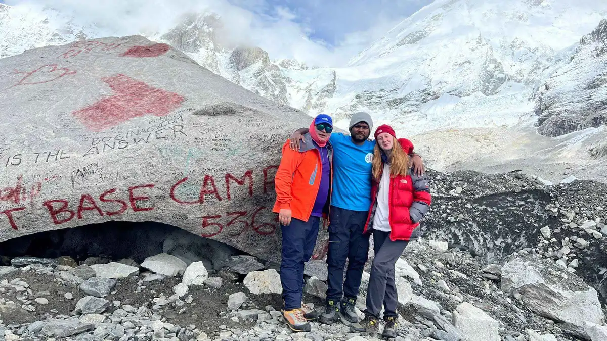 Three trekkers at the painted Everest Base Camp boulder on an Everest climbing tour in the Khumbu, Nepal