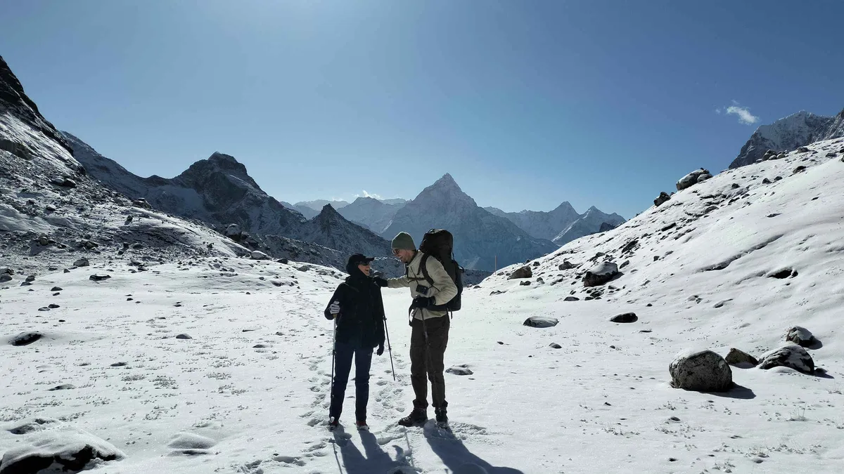 Two trekkers on a snowy trail with Ama Dablam behind on an Everest climbing tour over the Three Passes, Nepal